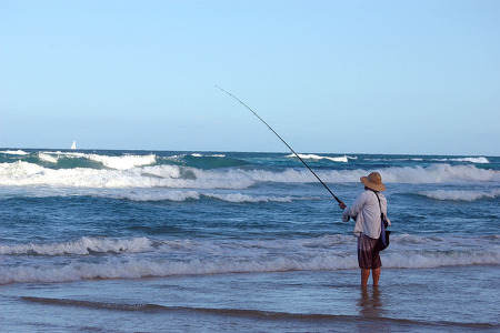man fishing in a white t shirt and a hat on the beach