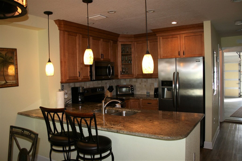 kitchen with three lights overlooking the countertop with seats on one side, and the kitchen on the other