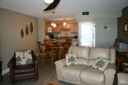 white couch and brown colored chair in living room with dining table and kitchen behind it